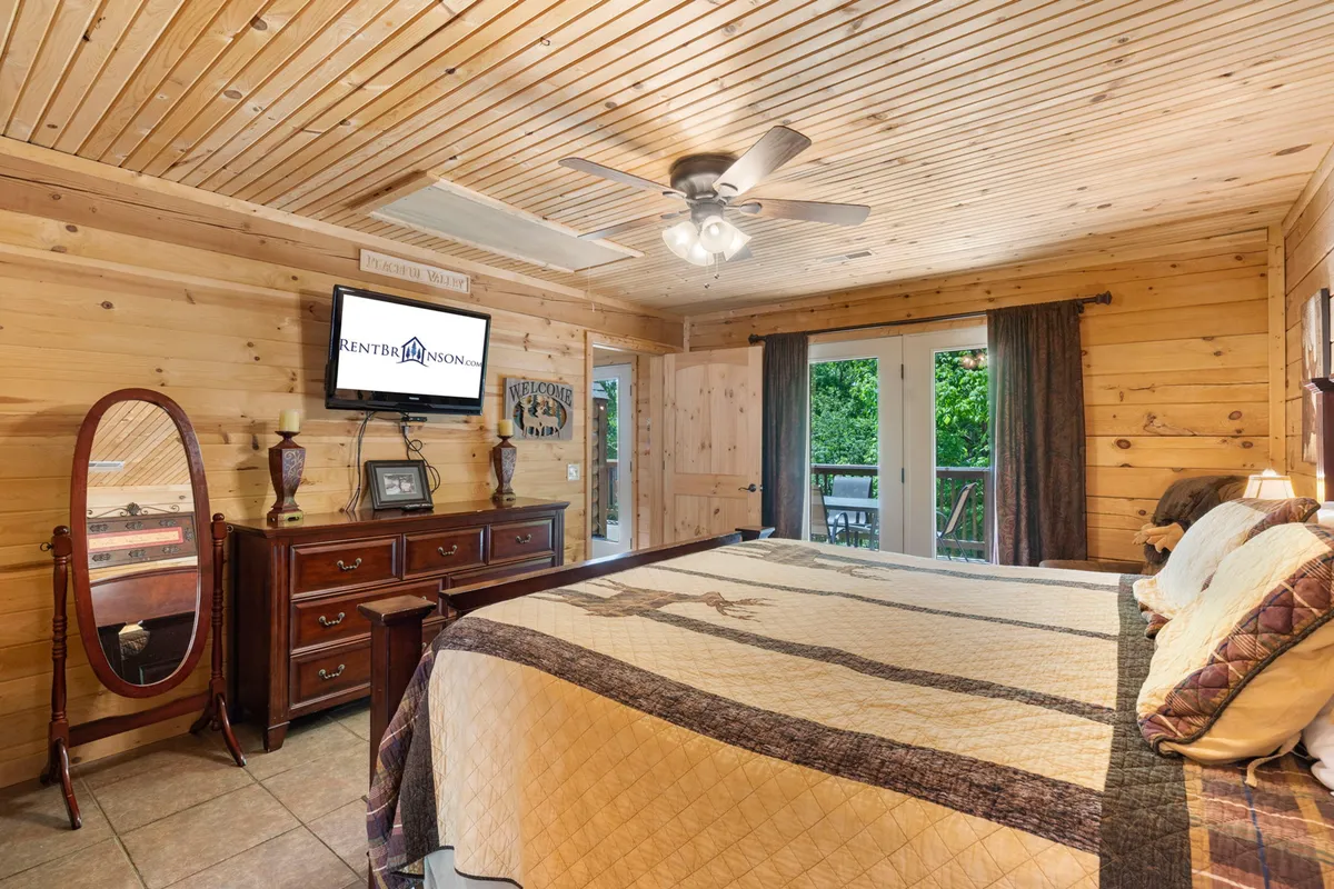 A comfortable bedroom with a stylish bed, wooden ceiling, dresser, mirror, and a TV. The room exudes a relaxed and homey ambiance, suggesting a perfect retreat for couples or solo travelers.