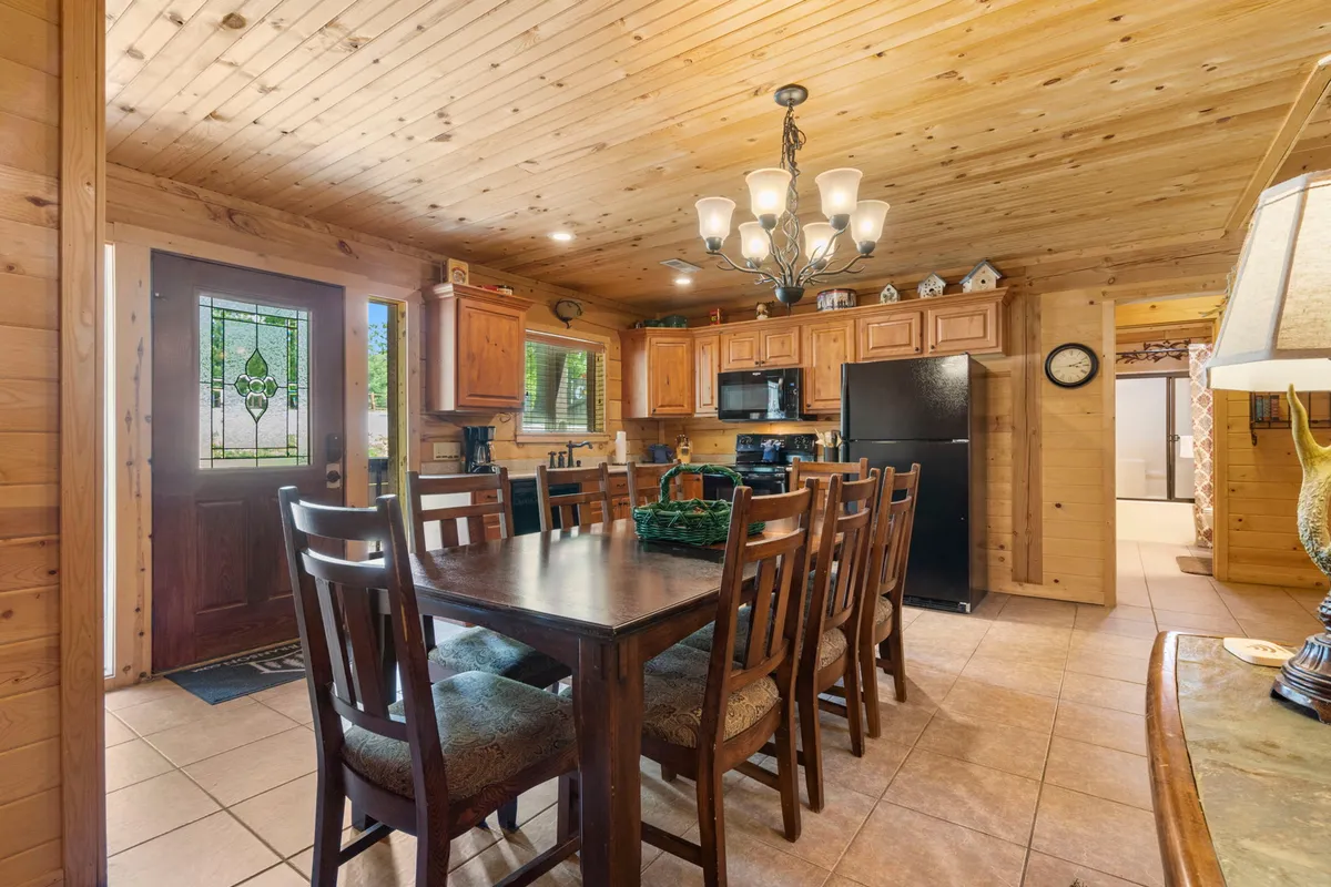 The focal point of this image is a generous wooden dining table set beneath a charming chandelier, with cabinetry and the front door nearby. The space radiates coziness and is clearly designed for family meals, social gatherings, and group activities like board games.