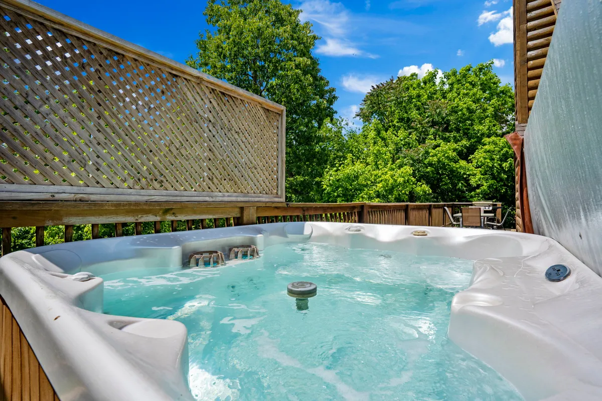 This image features a bubbling hot tub set on the back deck, surrounded by decorative lattice and lush greenery. The tranquil mood is enhanced by the natural setting, offering a private spot for relaxation and stargazing.