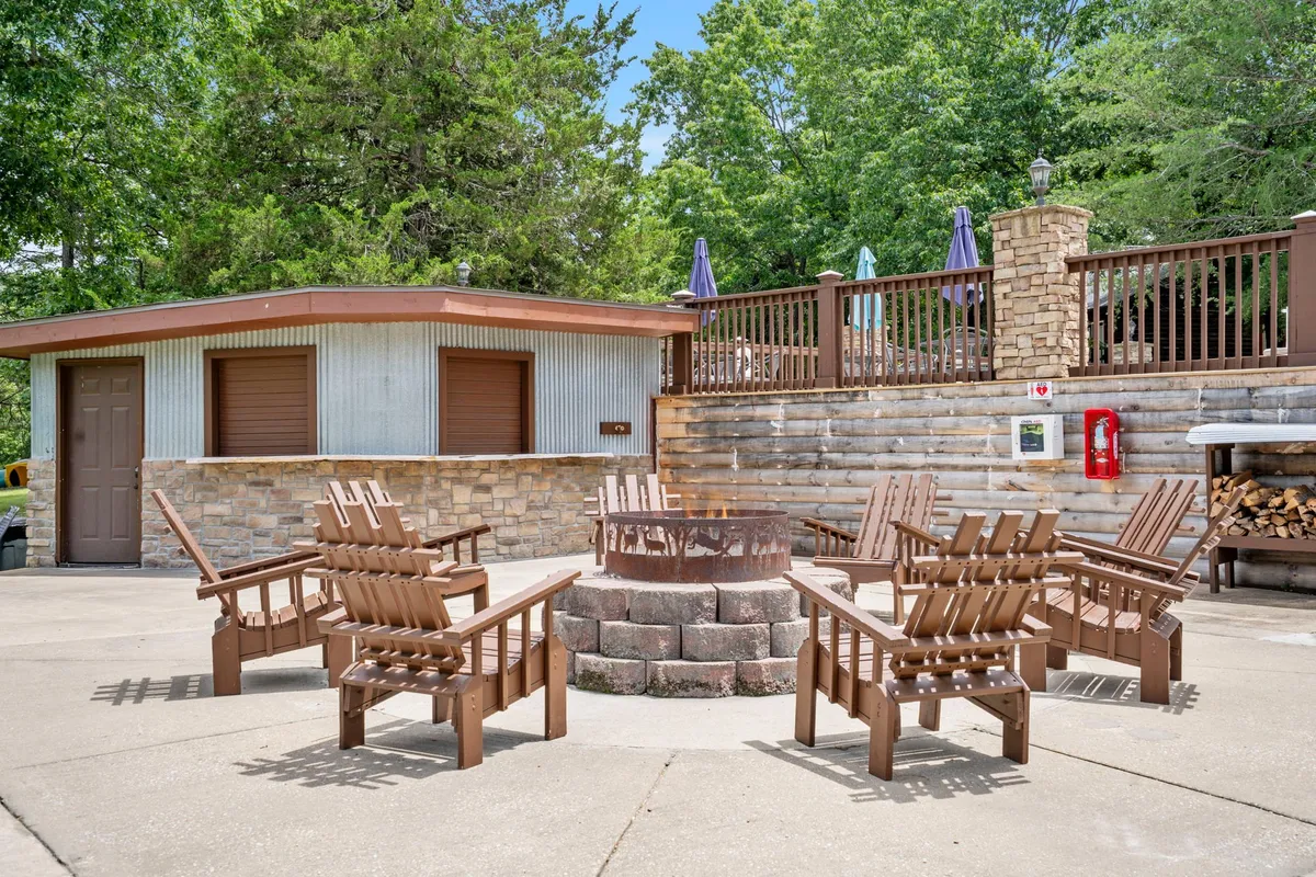 A cozy fire pit encircled by classic Adirondack chairs and a low stone wall, positioned amidst abundant greenery. The scene invites gatherings for storytelling, s’mores, and cozy conversations as dusk falls.