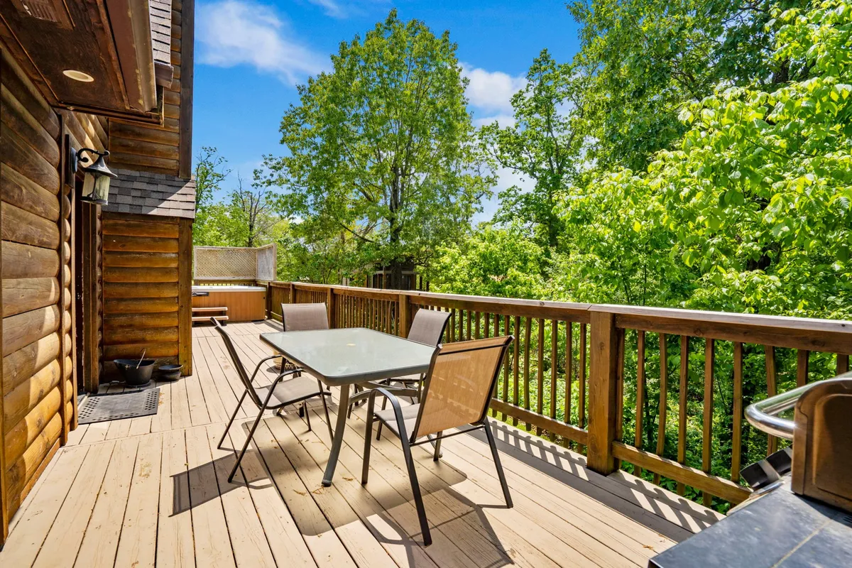 This photo captures the deck’s outdoor dining area with a glass table, comfortable chairs, a propane grill, and vibrant greenery as a backdrop. The inviting setting is perfect for enjoying meals or hosting summer barbecues while immersed in nature.