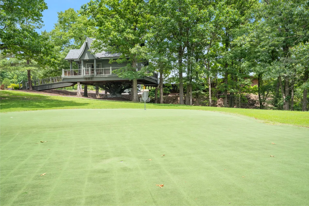 A peaceful golf green lies in the foreground, overlooked by an elevated house framed by surrounding trees. The tranquil setting hints at both relaxation and recreation, making it ideal for those seeking a blend of sporting action and serene views.
