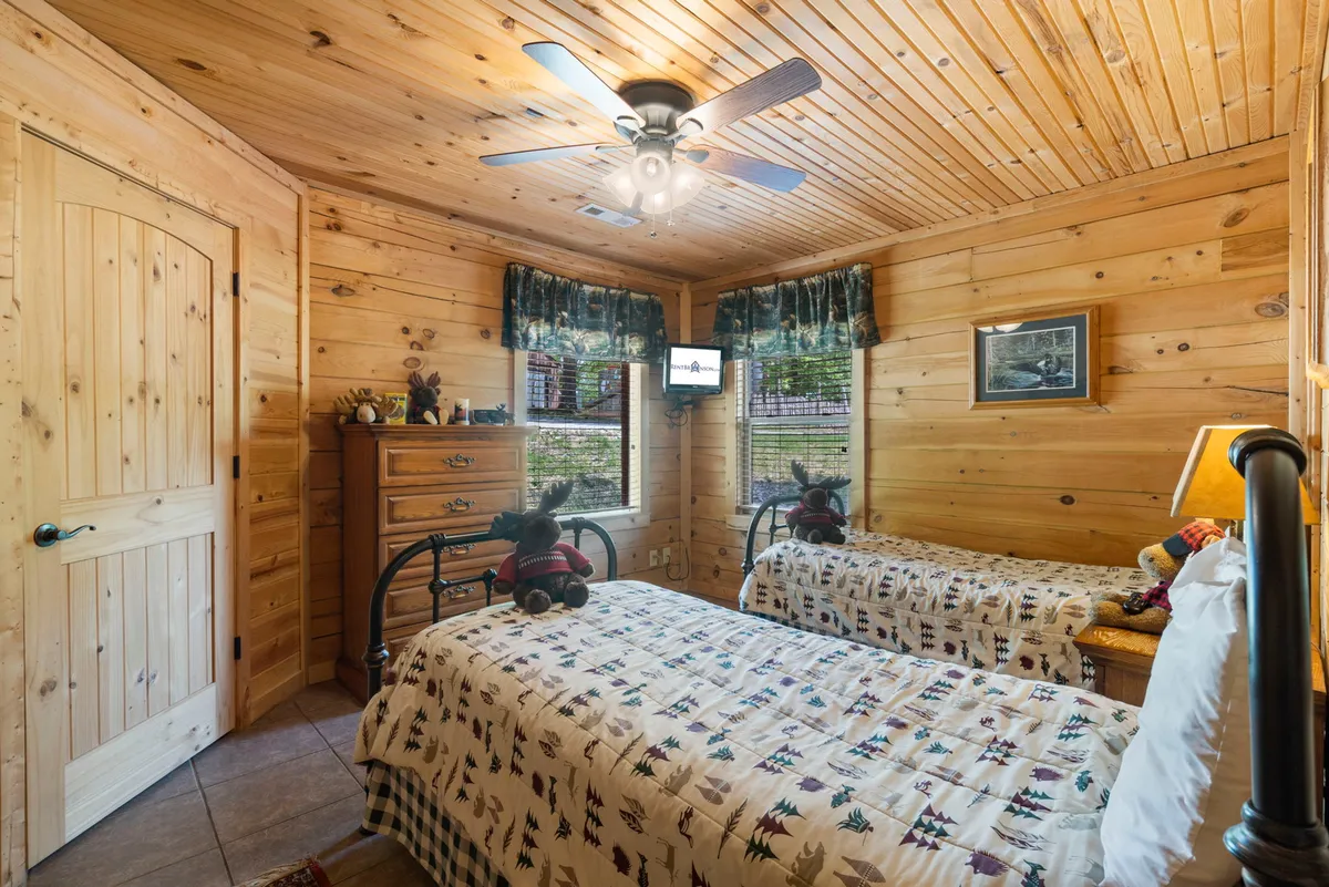 A cheerful bedroom with twin beds, decorative teddy bears, and a window view that lets in ample sunlight. The playful décor and inviting setup make it an ideal space for children or friends sharing the room.